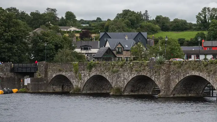 Four stone arches of the old Killaloe bridge over the Shannon, with its steel span on the left and houses beyond.