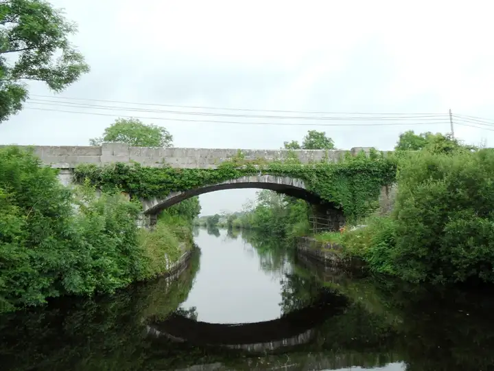 Eine efeubewachsene steinerne Straßenbrücke überspannt den Jamestown-Kanal oberhalb von Albert Lock, ihr Bogen spiegelt sich im stillen Wasser.