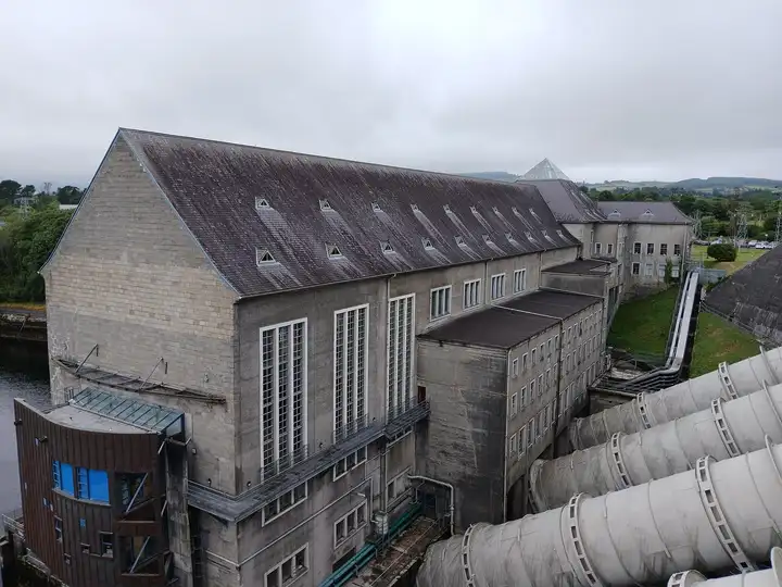 The large main building of Ardnacrusha power station stands beside the tailrace, with its huge penstock pipes in the foreground.