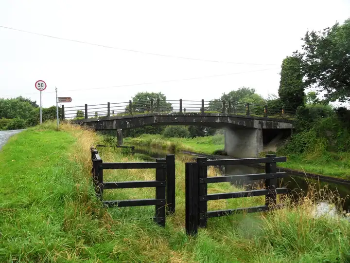 Becans Bridge, a plain concrete road bridge over the canal near Rahan, with black timber barriers on the grassy towpath and a signpost pointing to Rahan.