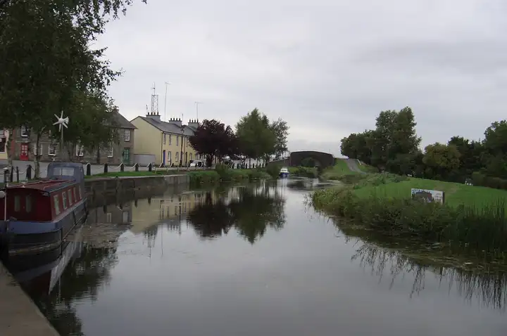 La rangée de maisons de Robertstown au bord du canal se reflète dans l’eau calme, avec une péniche rouge et bleue amarrée à gauche et un pont en dos d’âne au loin.