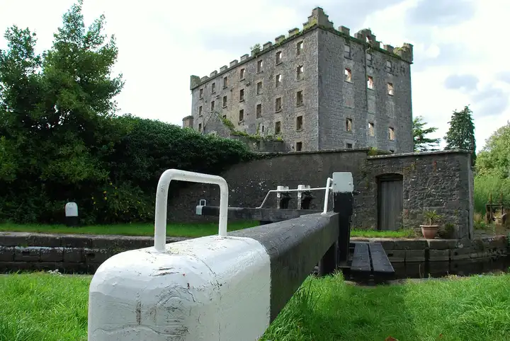 The white-tipped balance beam of Levitstown Lock leading towards the tall, roofless stone shell of the old malt mill.