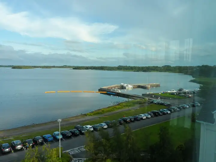 Hodson Bay harbour seen from above, with boats inside the L-shaped breakwater, a line of yellow floats on the lake and wooded shores beyond.